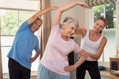 Elderly couple in the comfort of their own home doing fitness training with the support of a female personal trainer.