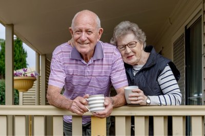 Senior couple smiling and having their coffee outside on their porch