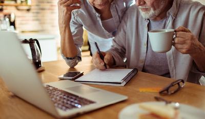 Senior couple in front of a computer with pen and paper doing budgeting.