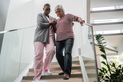 A female senior walking down stairs with the help of a younger adult.