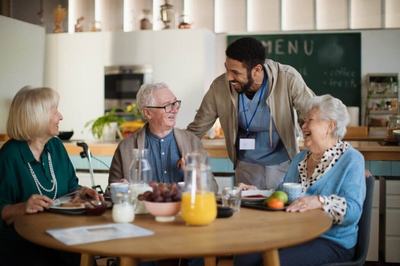 Multiple seniors engaging with assisted living facility staff in a communal space.