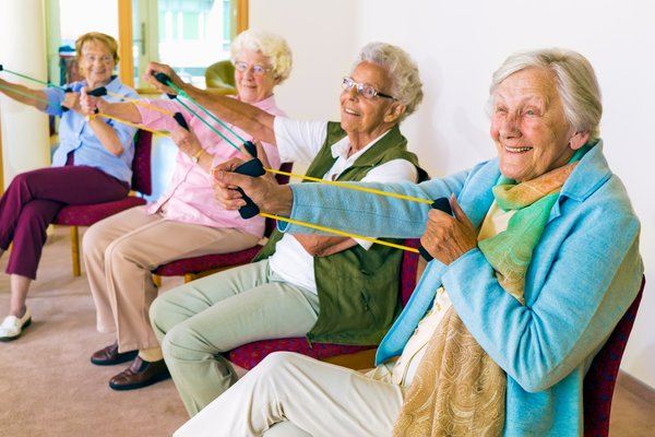 Four seniors sitting inchairs and working out with stretch bands
